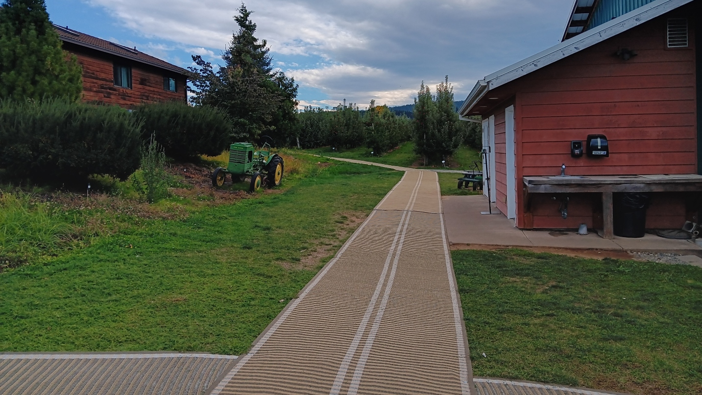 Long rubber mats on grass with barns on either side and a small green tractor