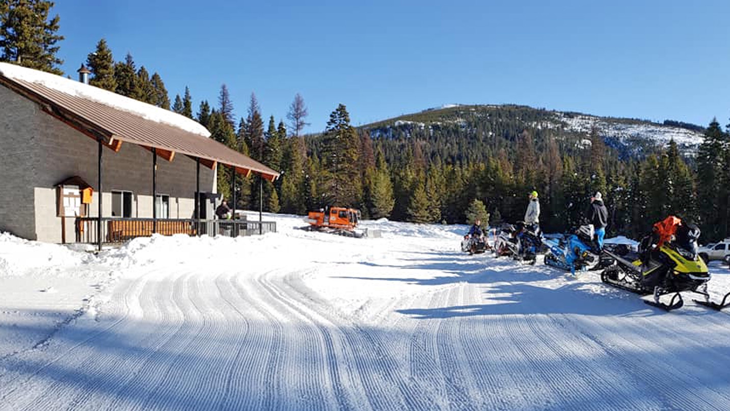 People outside a building with their snowmobiles.