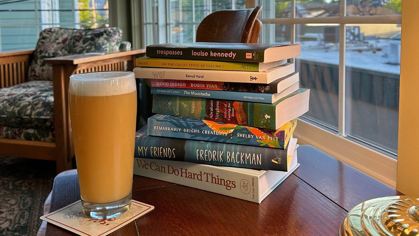 A stack of books on a table with a large glass of beer.