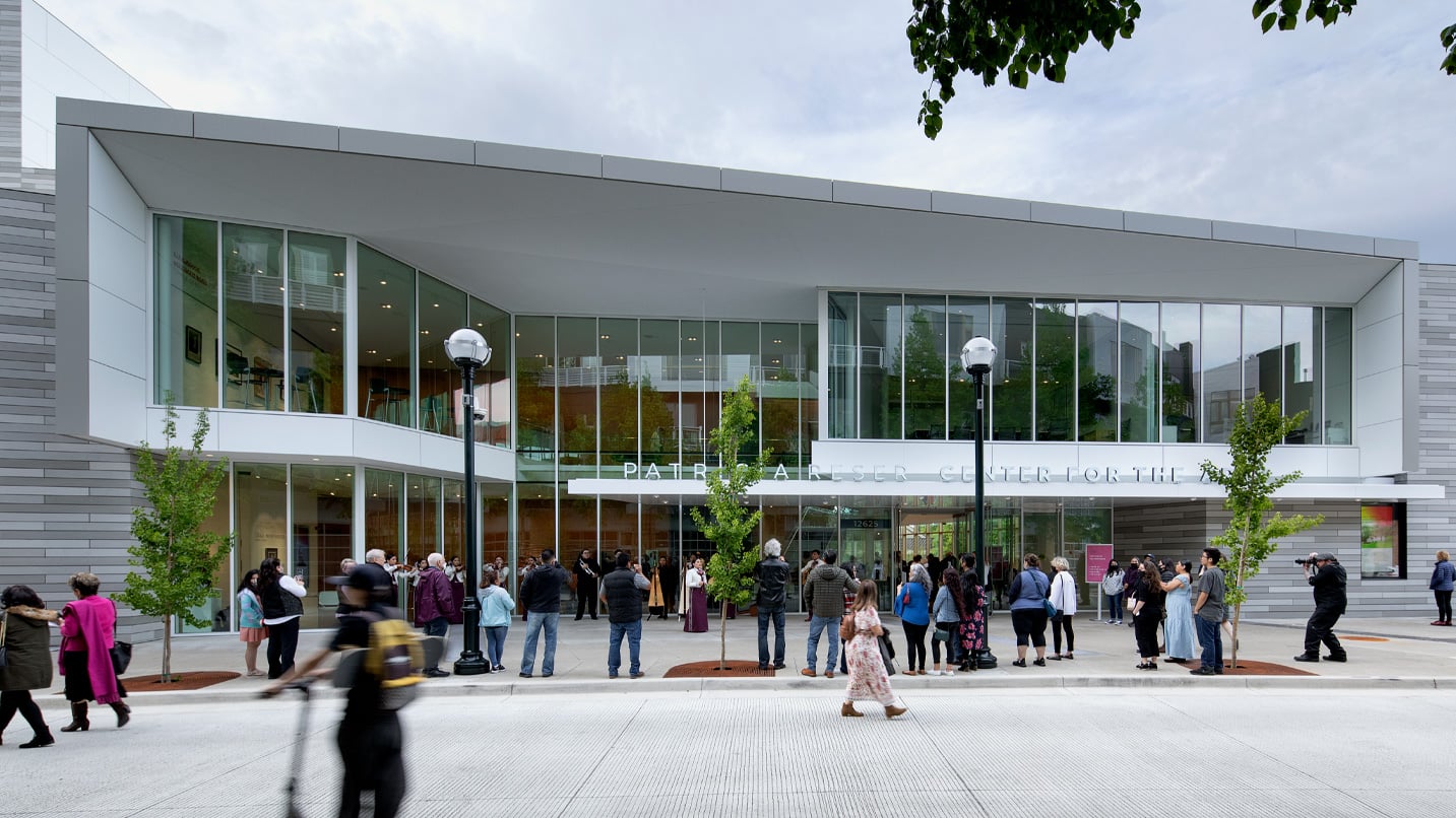 People walking in front of a modern-glass building performance center.