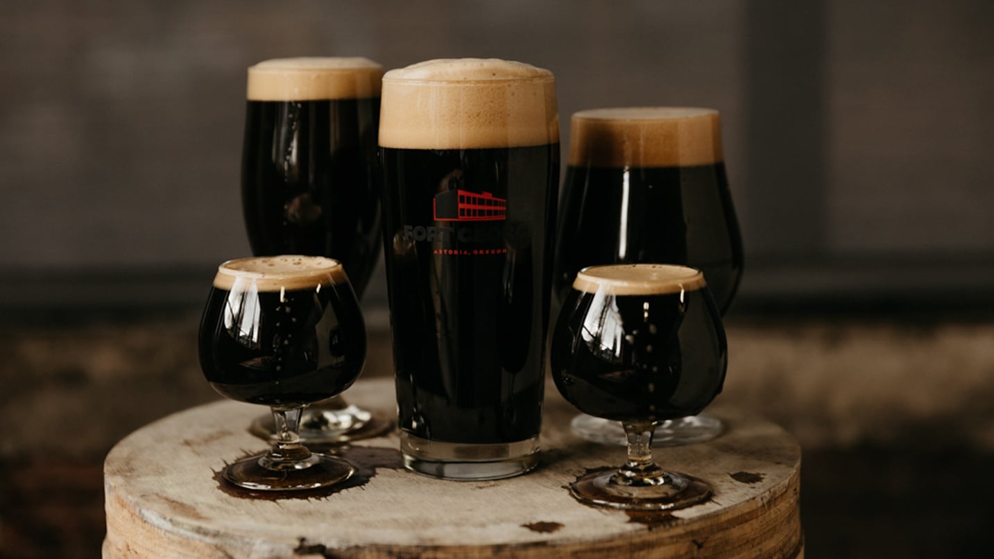 Dark beer in several styles of glasses. The center glass features Fort George Brewery's logo.