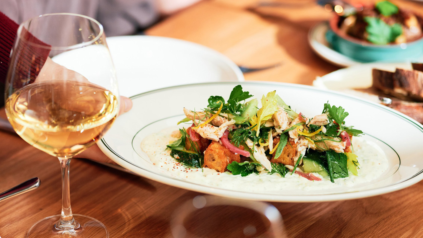 A plated dish being set down on a table with a glass of wine.