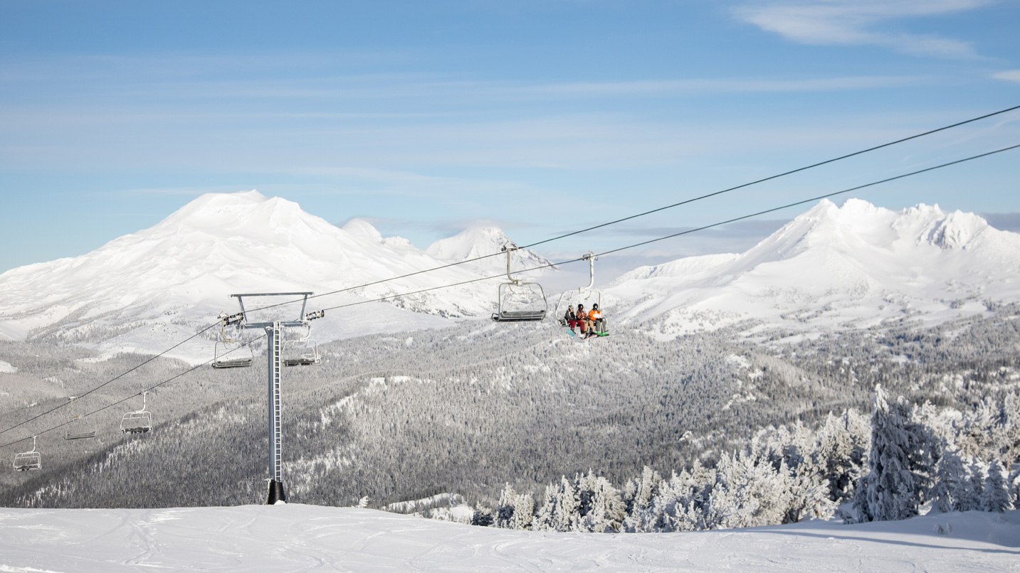 A ski lift with snow capped mountains in the background.