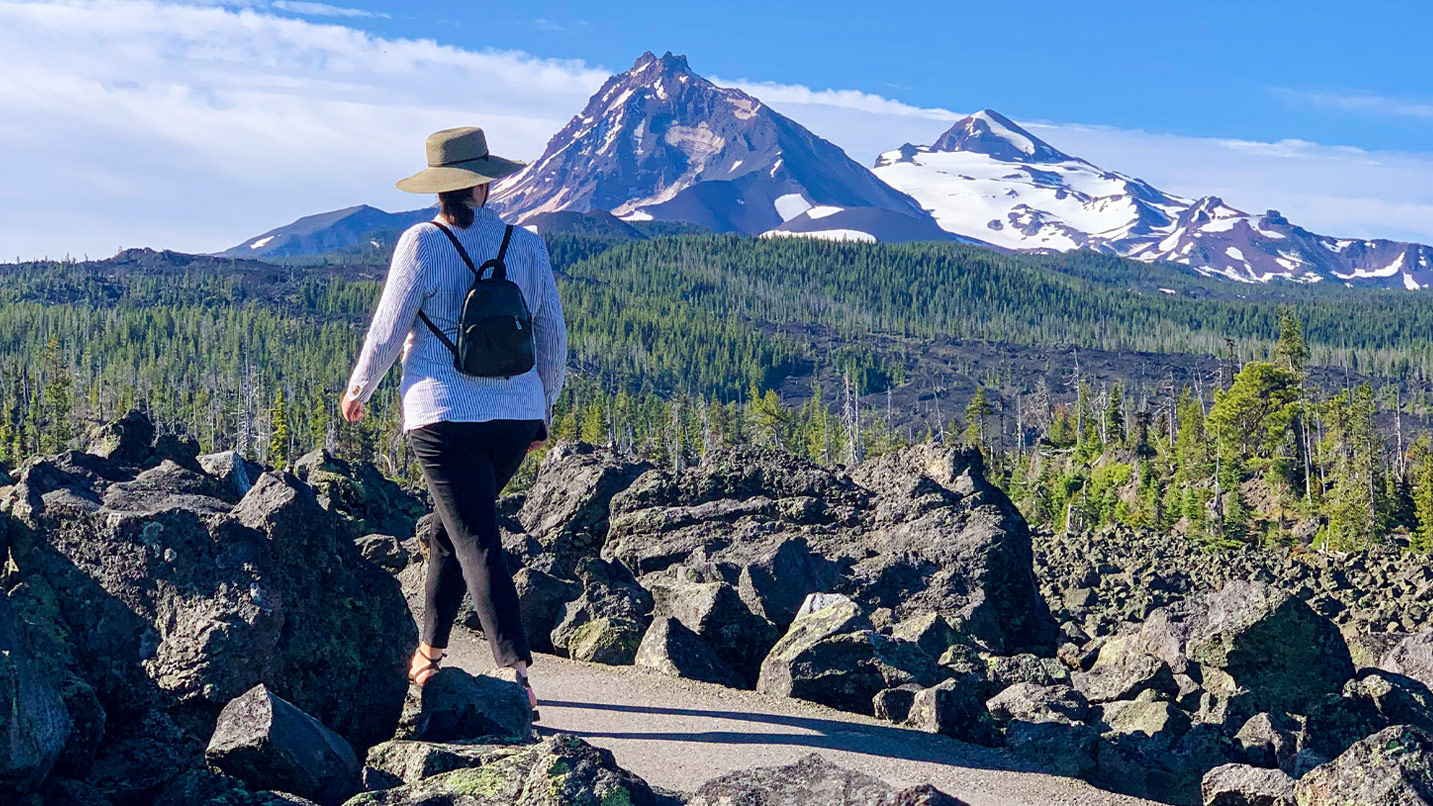 A woman walks along path surrounded by mountain views and lava rocks.