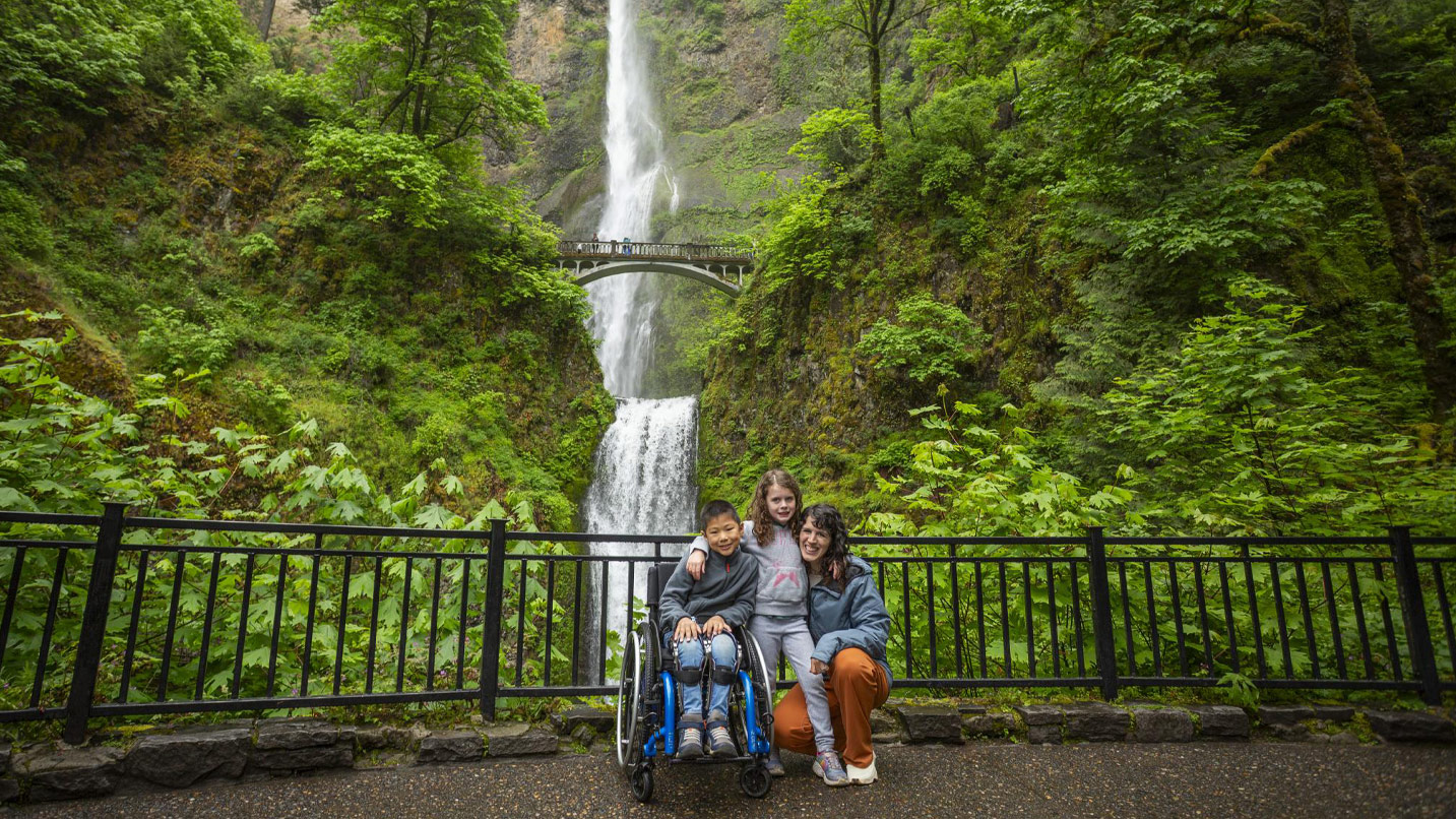 A woman and two children, one in a wheelchair, in front of Multnomah Falls.