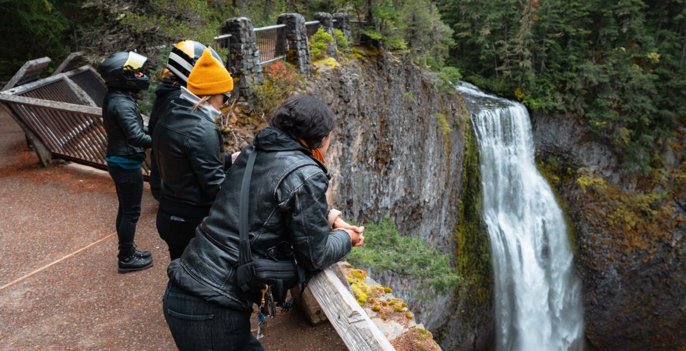 Four motorcyclists stop to enjoy the waterfall views on a fall day.
