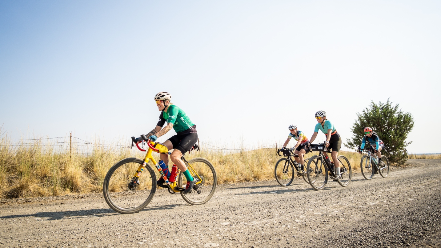 Four people ride bikes and smile on a bumpy gravel road