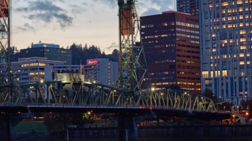 Bridge over a river at night, with tall buildings lit up at dusk