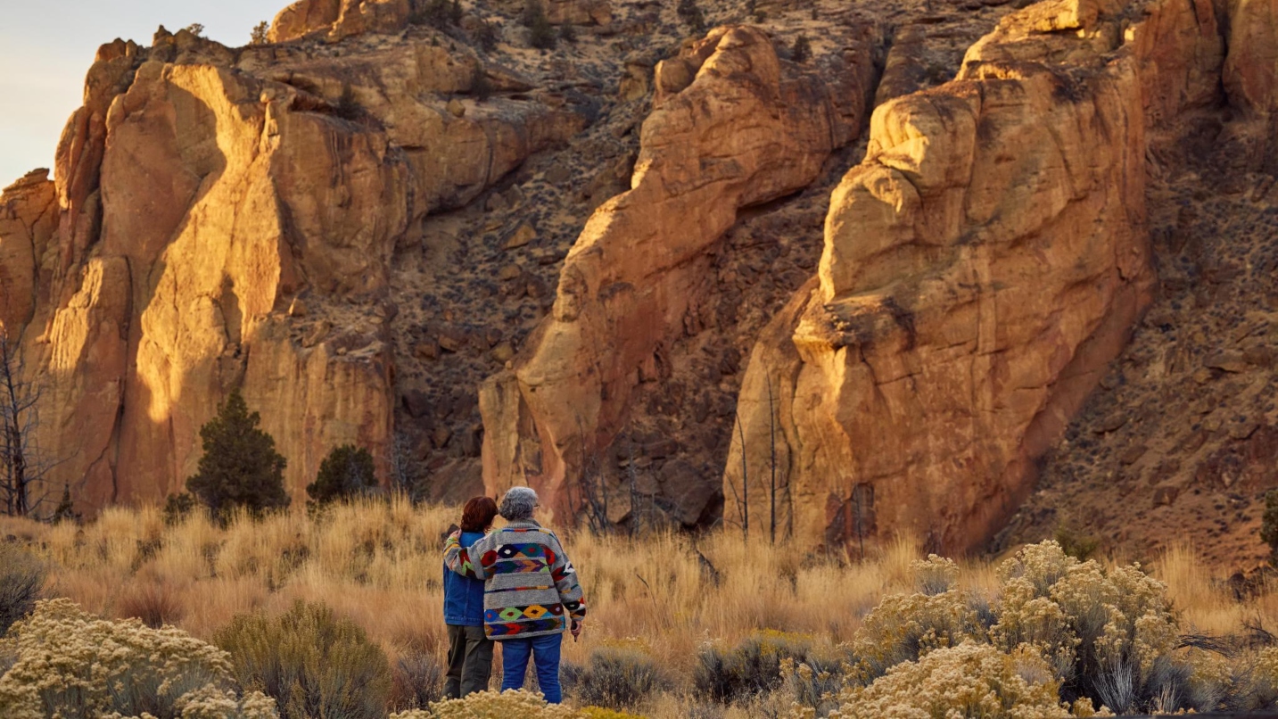 Two people stand among tall grasses looking at large rock walls