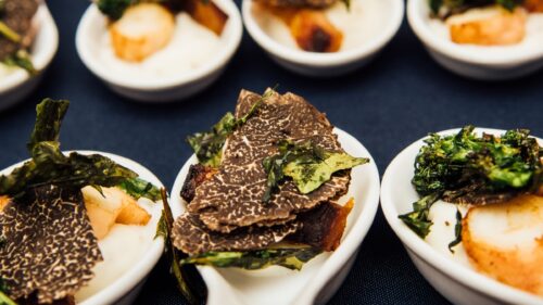 Several white spoons in a row with shaved black truffles and other ingredients