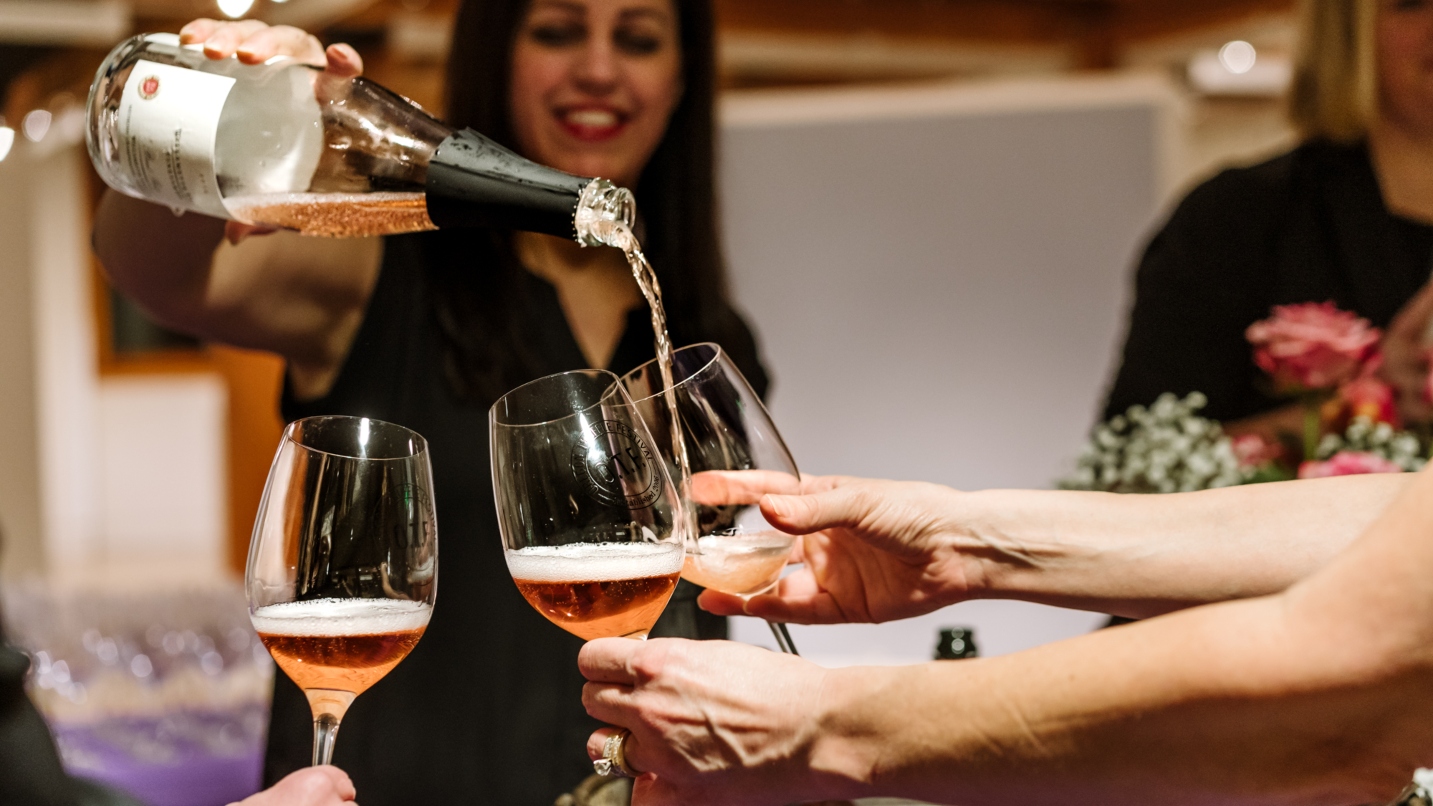 Hands hold three glasses of pink sparkling wine being poured by a woman