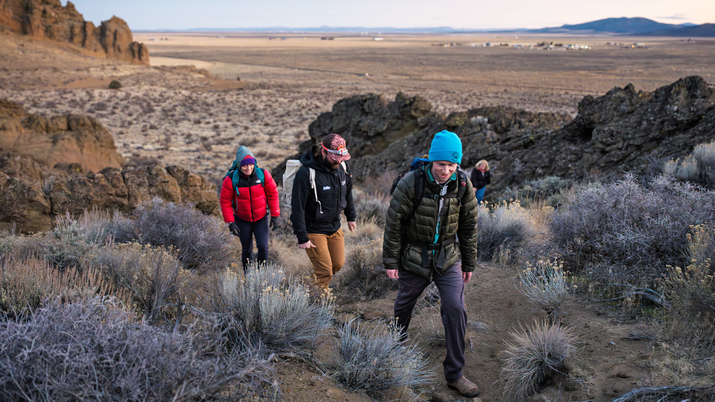 A group of people hiking up a path with a large rock formation in the background.