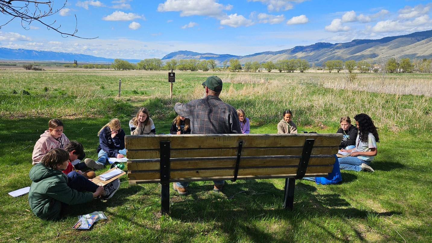 A group of kids sit in the grass backing up to a restored natural area.