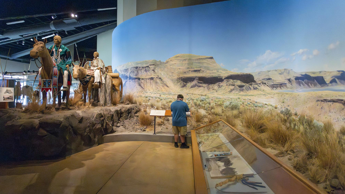 A person looks at an exhibit that includes people on horseback and a collection of artifacts.