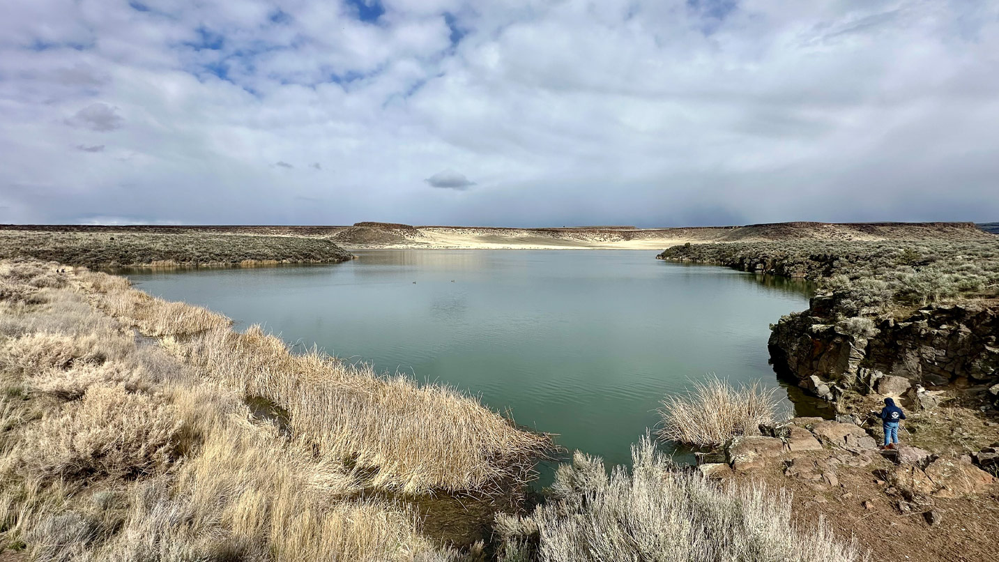 Rocks and sagebrush surround a small body of water.