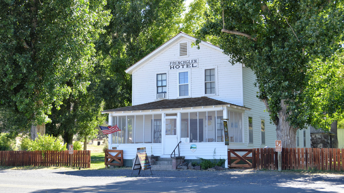 A two-story historic wooden white building with an enclosed front porch.