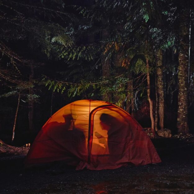 Two silhouettes of people in an orange tent at night in a forest