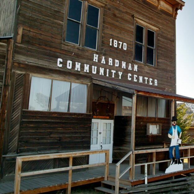 Wooden two-story structure with white sign that says 1870 Hardman Community Center