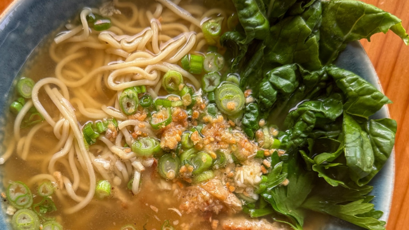 Close-up bowl of noodles, soup, green onions and spinach on a table