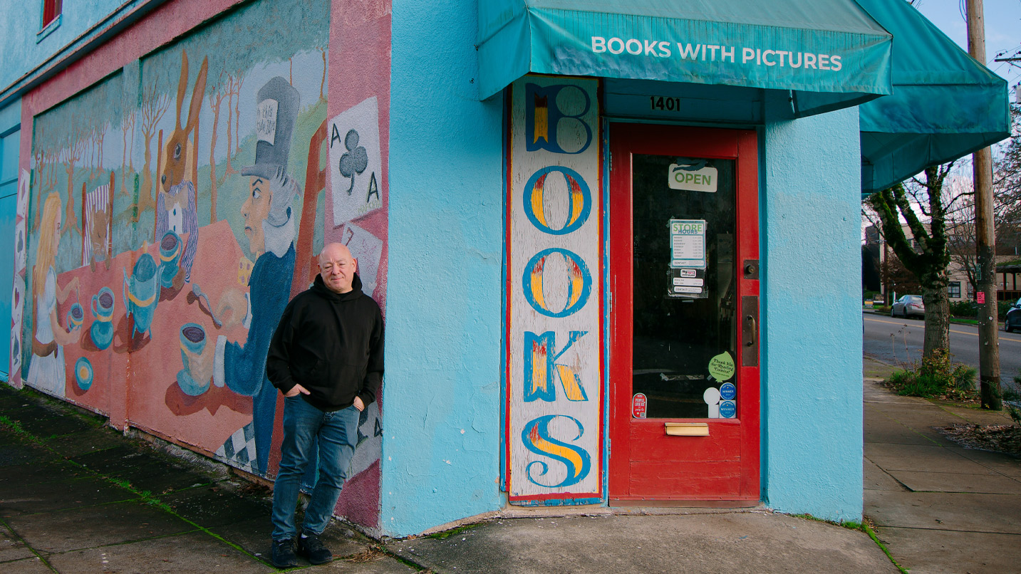 A man stands in front of a brightly painted mural on the side of a store.