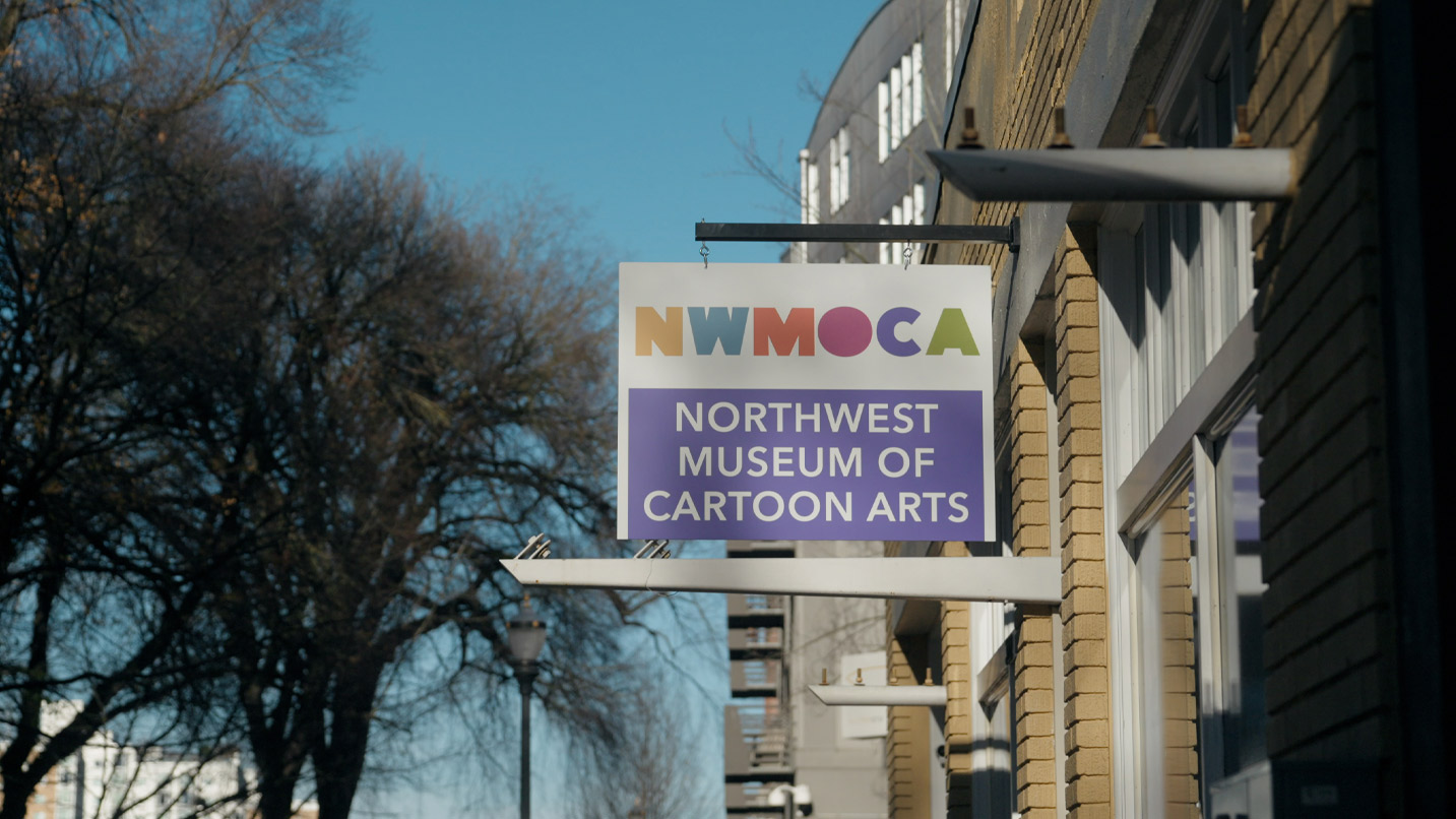 A sign hangs from an outdoor building saying Northwest Museum of Cartoon Arts.
