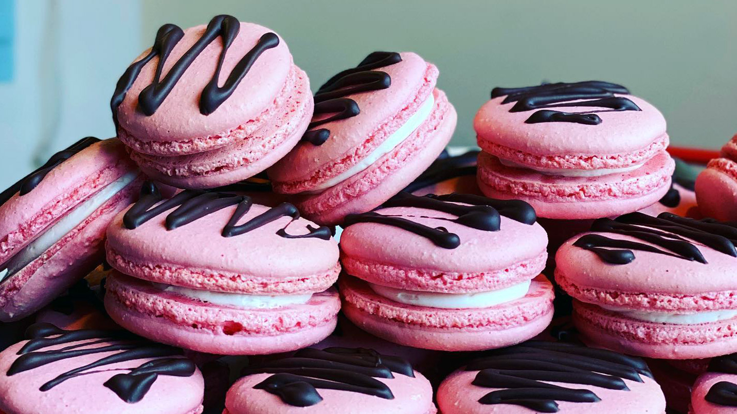 Several pink macarons with chocolate drizzle stacked on top one one another.