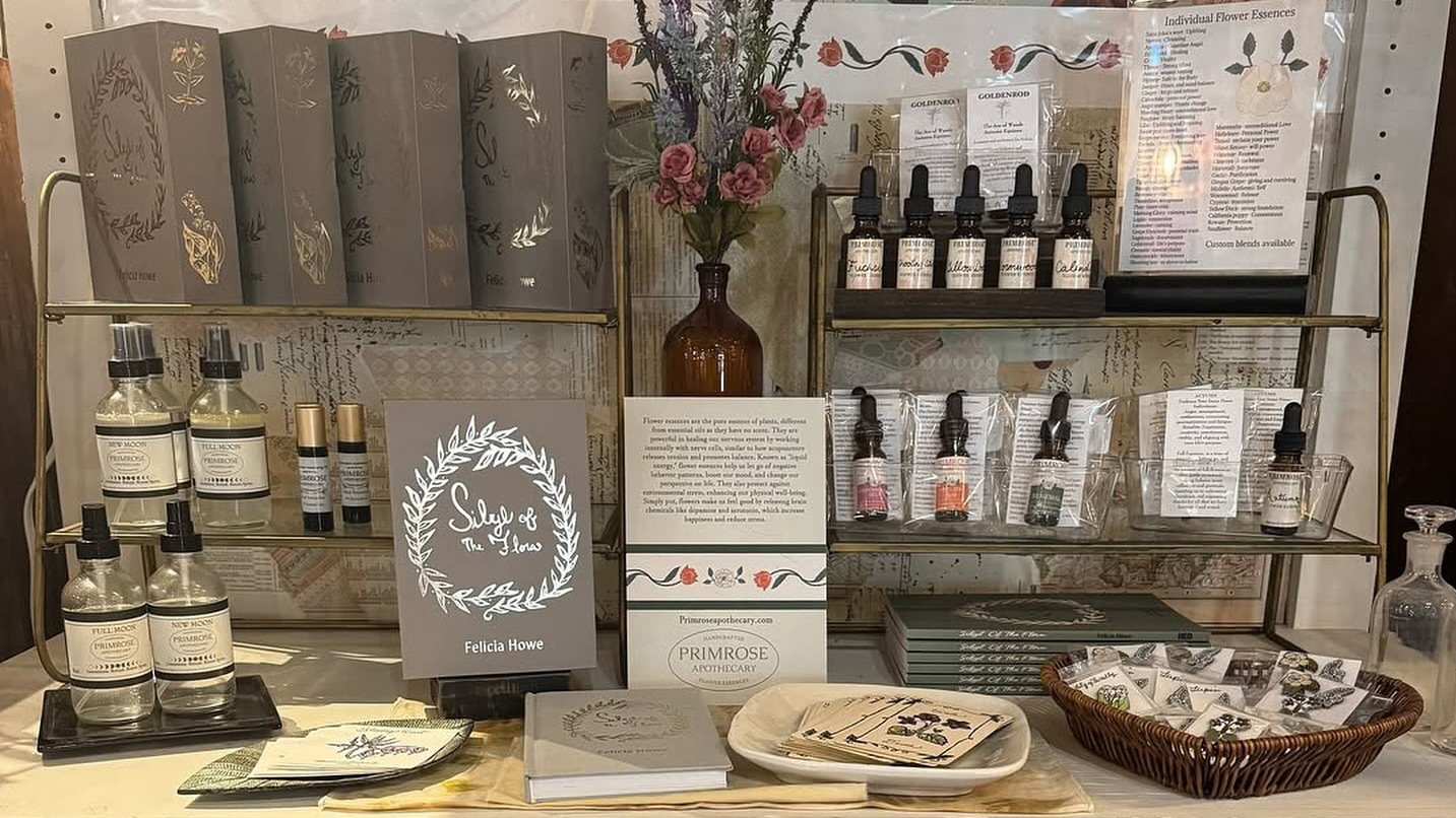 Beauty serum bottles of various sizes on a small display. Pictured also are signs (unreadable) and other for sale items like pins and journals.