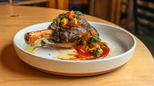 Modern white ceramic dish on table with leg of meat and sauce plated in an artful way
