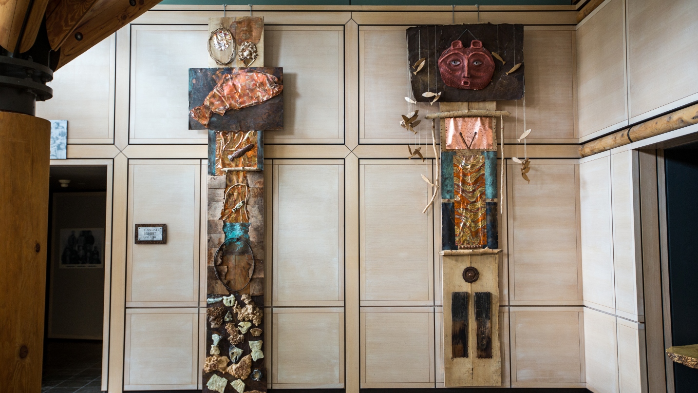 Two tall Native American sculptural pieces of art reach up to the ceiling in a museum