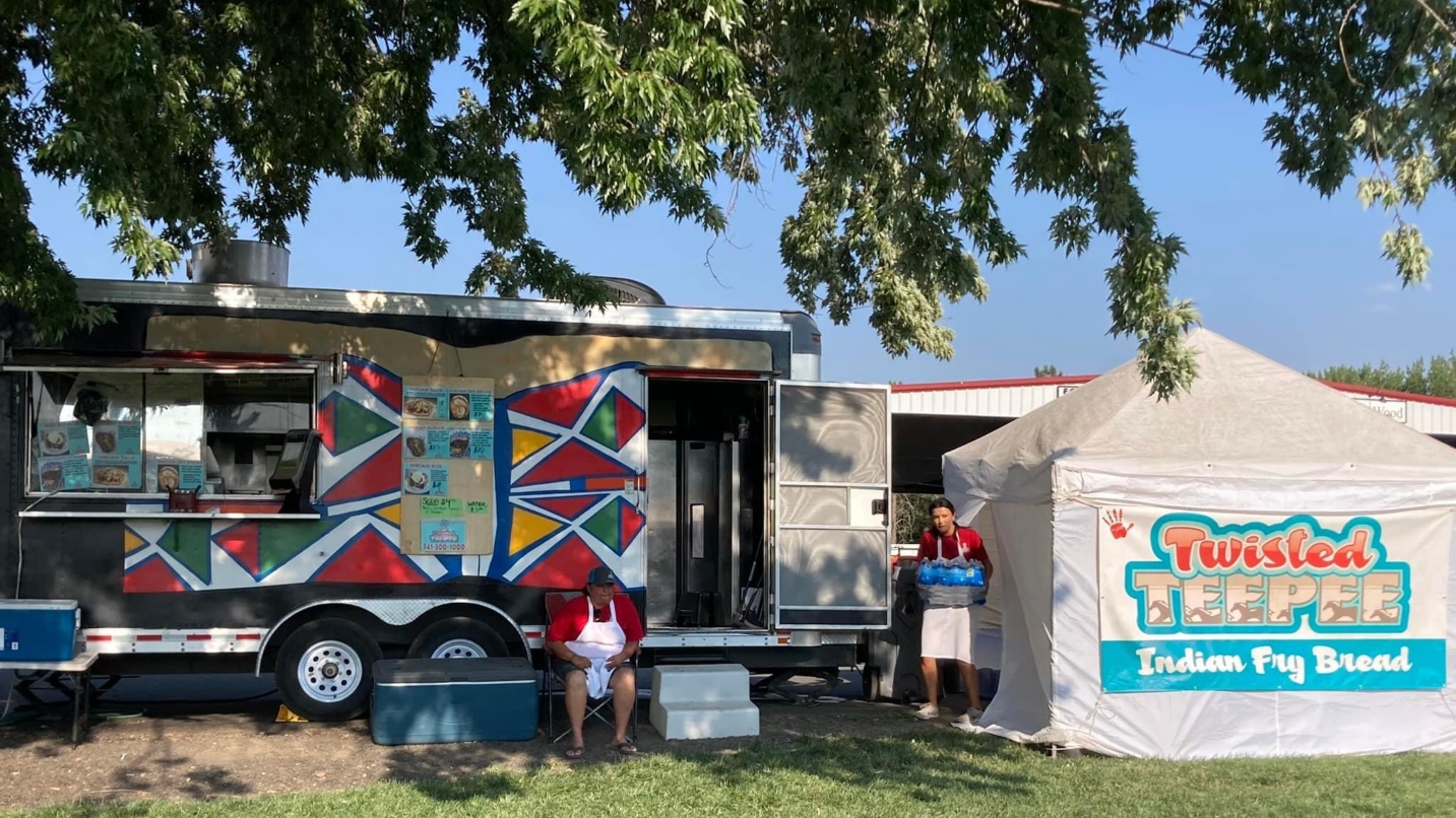 Two people in front of a colorful food cart and white tent with the name Twisted Teepee/Indian Fry Bread displayed
