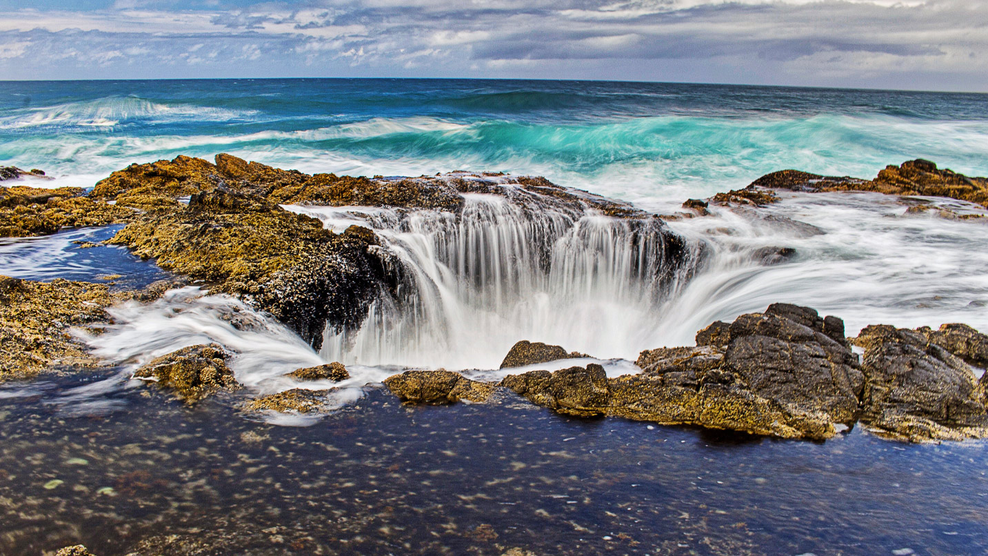 A natural sinkhole on basalt rock. Water from the ocean rushes in as a wave comes in.