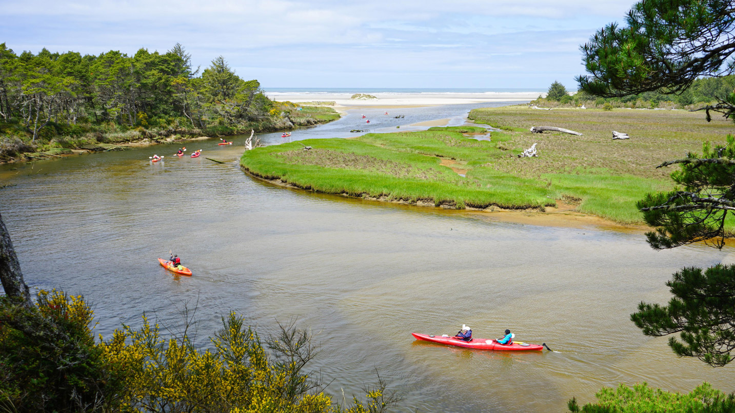 A few kayaks head down a river towards the ocean.