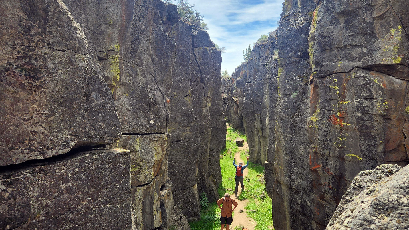 Two people walk between towering rock columns.