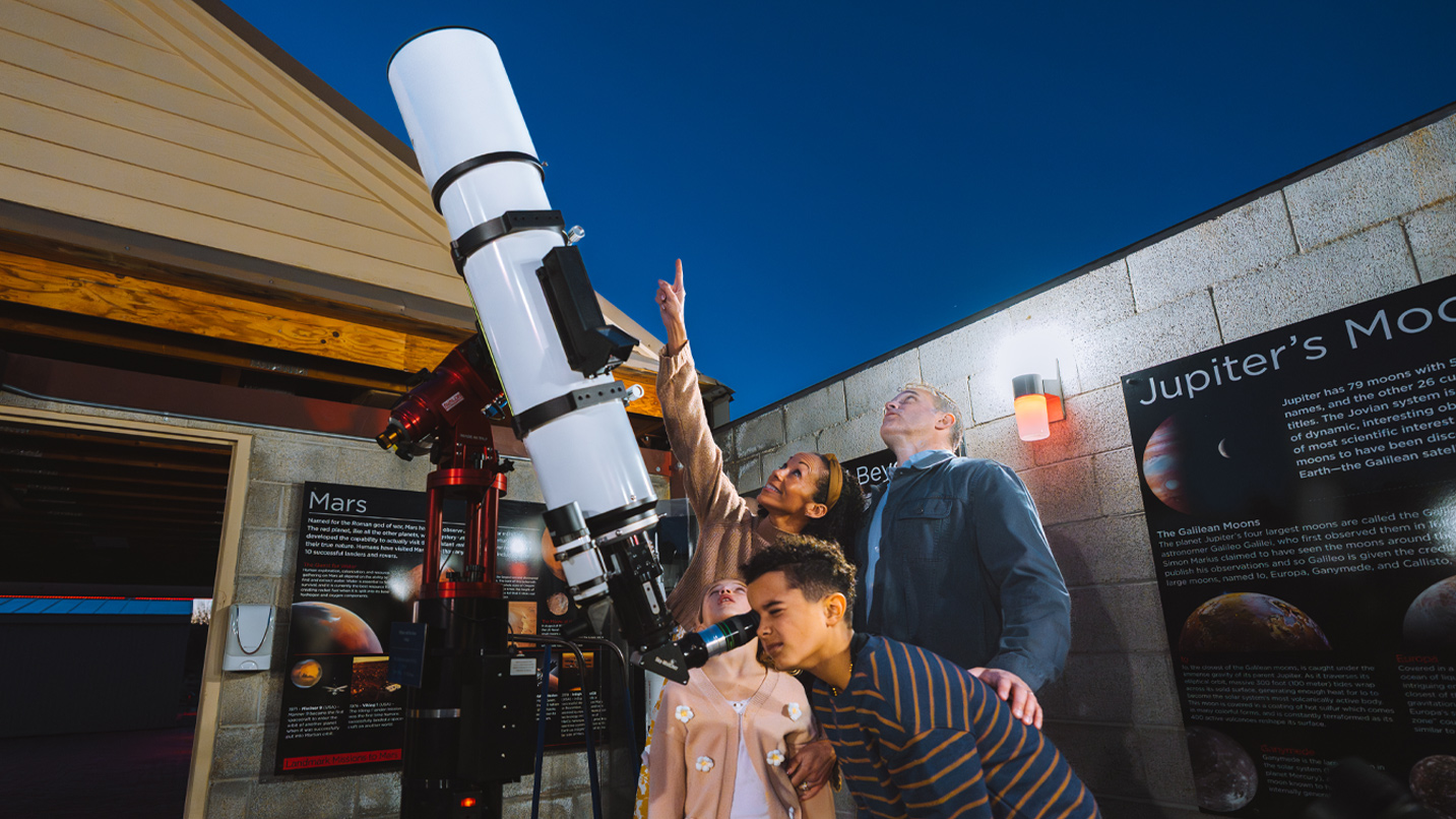 People look through a large outdoor telescope.