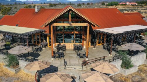 Back patio of a large vineyard property. Several tables and umbrellas for outdoor seating.