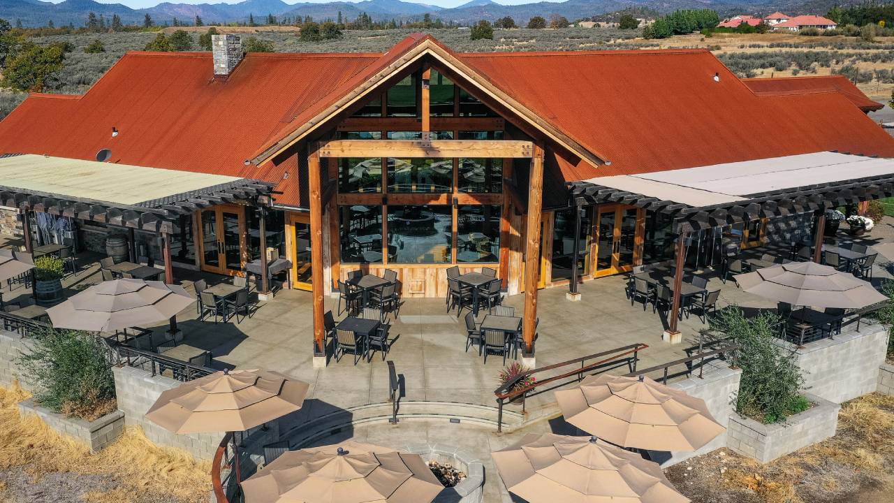 Back patio of a large vineyard property. Several tables and umbrellas for outdoor seating.
