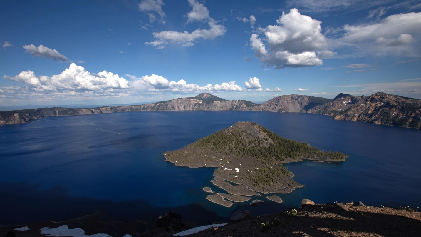 Large blue lake in a caldera with a small island in the middle, blue sky and white clouds
