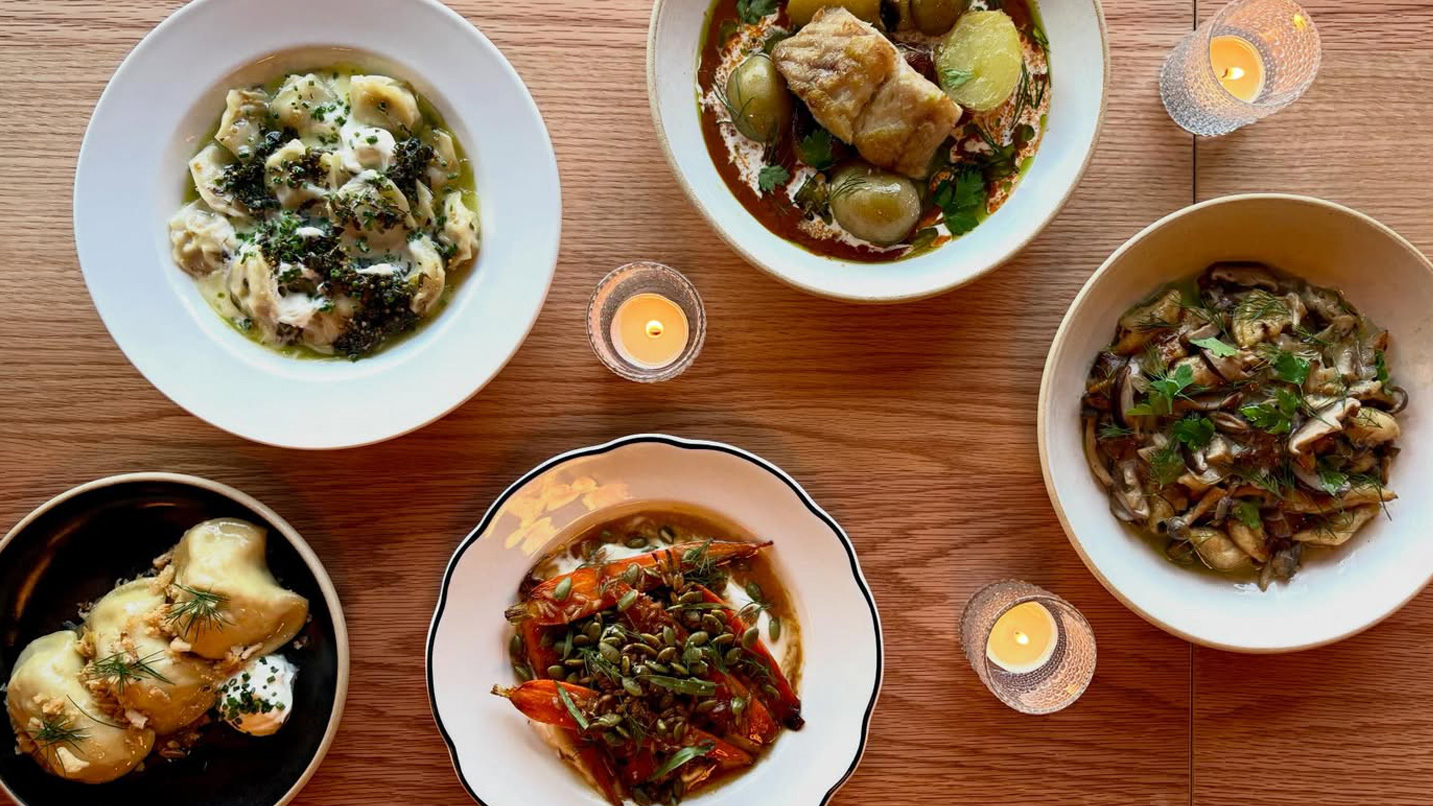 Several plates of Slavic food, including braised carrots, dumplings and stewed fish and vegetables.