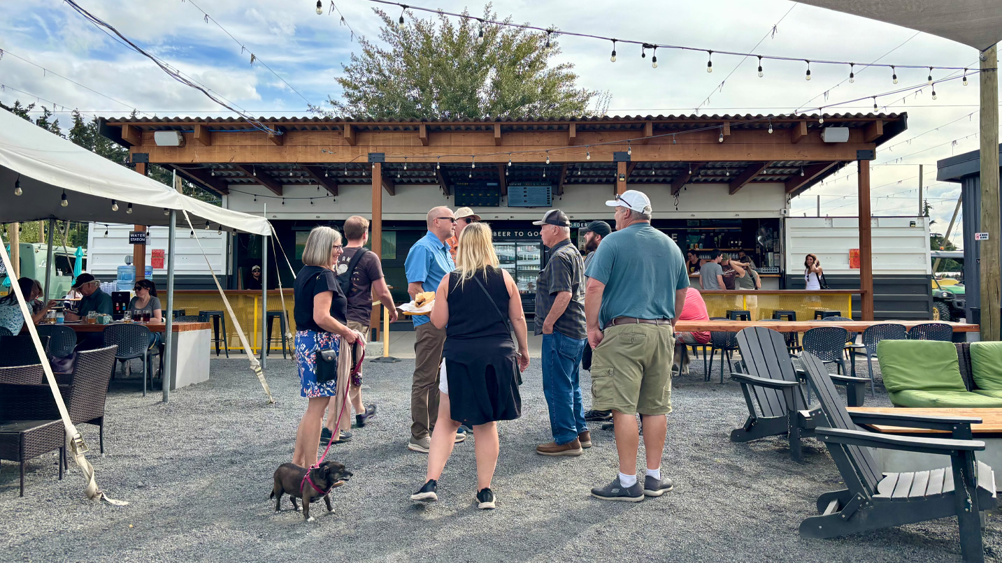 A large group of people stand around talking in an outdoor beer garden.