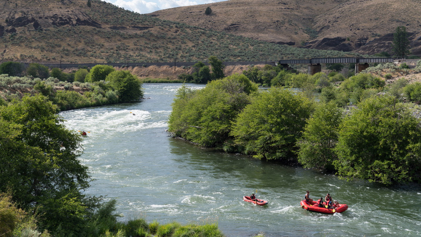 A small raft and kayakers along the Deschutes River.