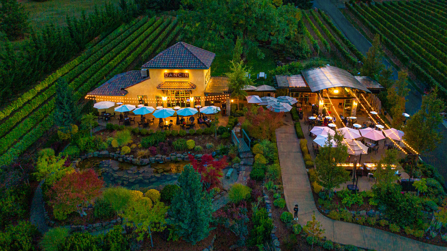 An aerial photo showing a winery at night with outdoor lights, umbrellas and vineyards.