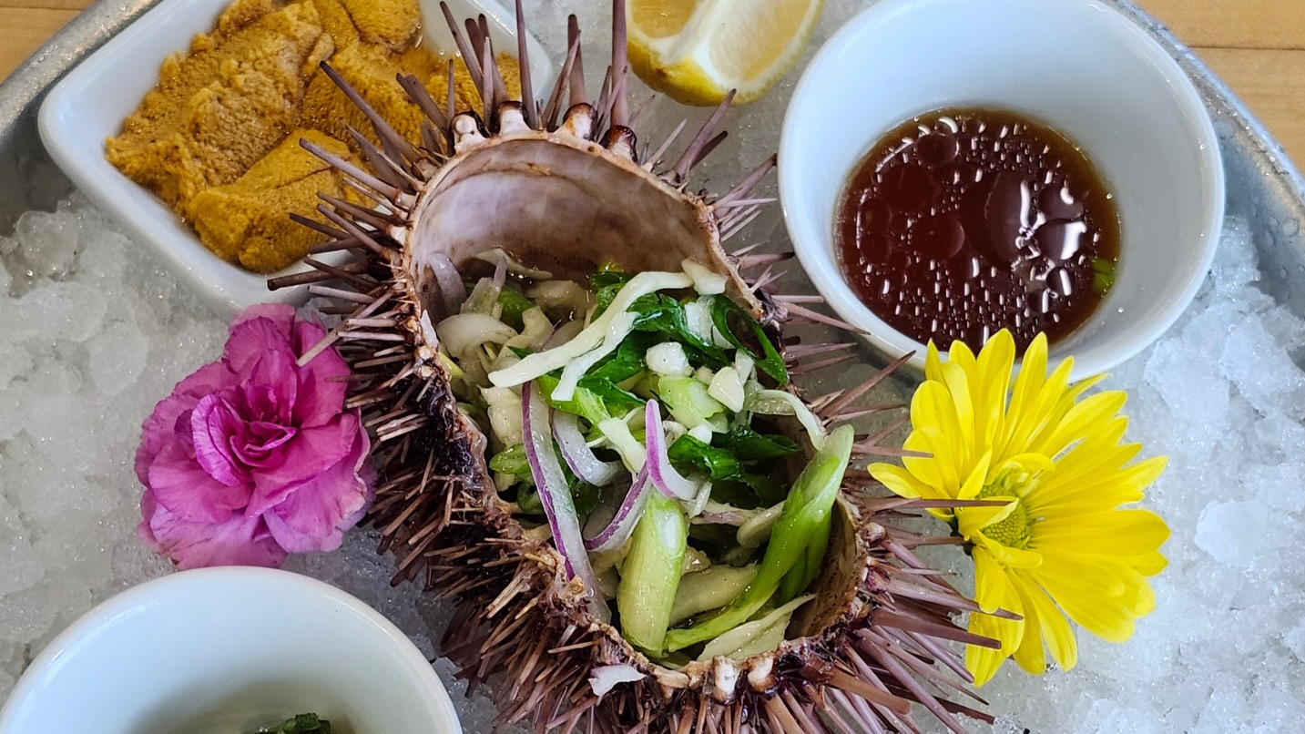 An urchin slided in half with food inside set on a plate with condiments.