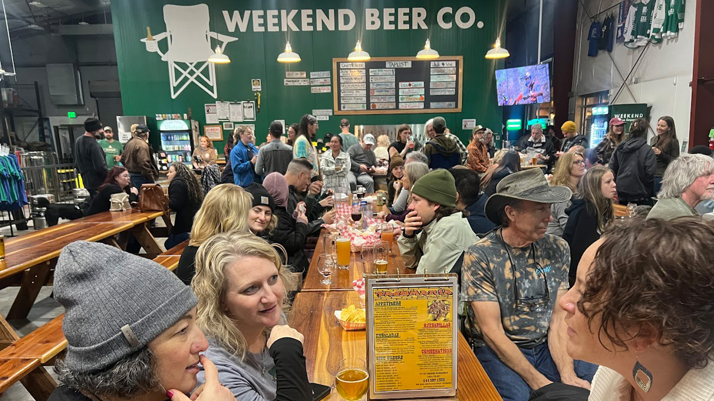 People sit at long tables in an indoor beer hall.