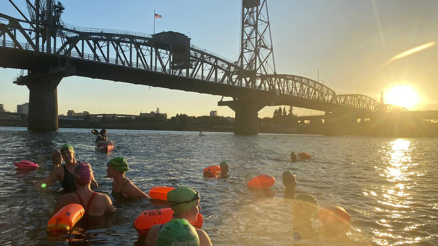 Several people swimming in the Willamette River as the sun sets over the Hawthorne Bridge in Portland.