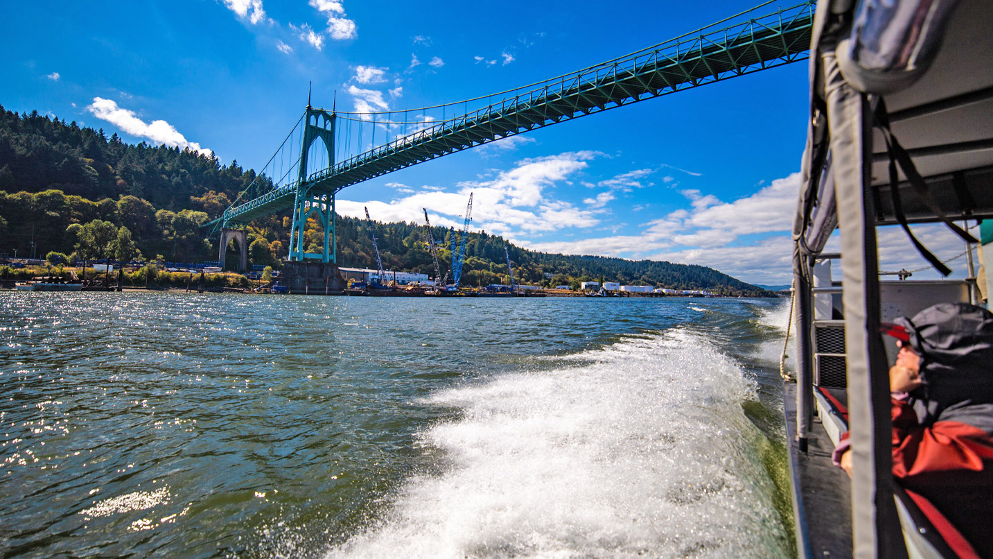A jetboat goes under a large bridge.