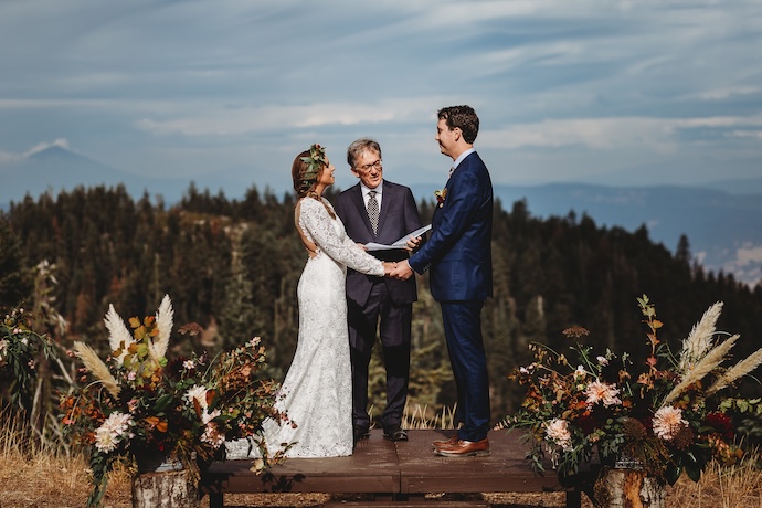 A couple exchange wedding vows in an outdoor venue with wildflowers and distant mountain views. 