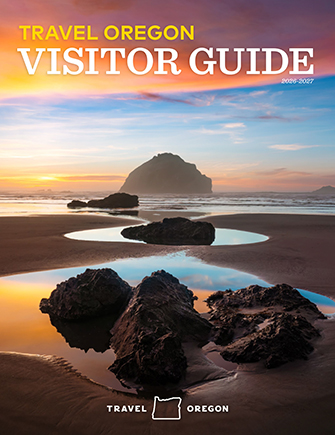Visitor Guide cover featuring a sunset view of the Oregon Coast with water reflections and rocks in the foreground and background.