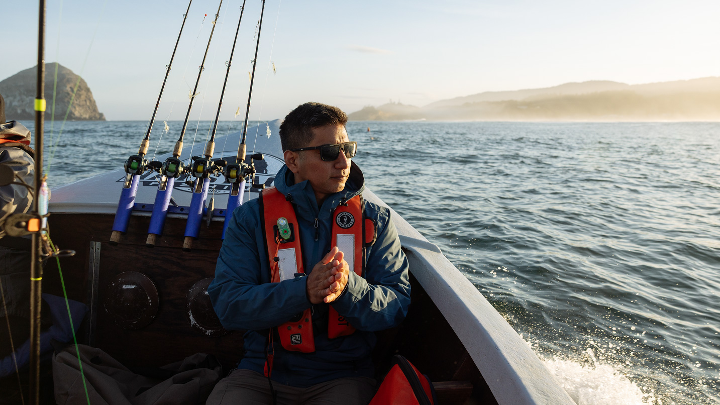 A person on a boat with a large rock out in the distance in the ocean.