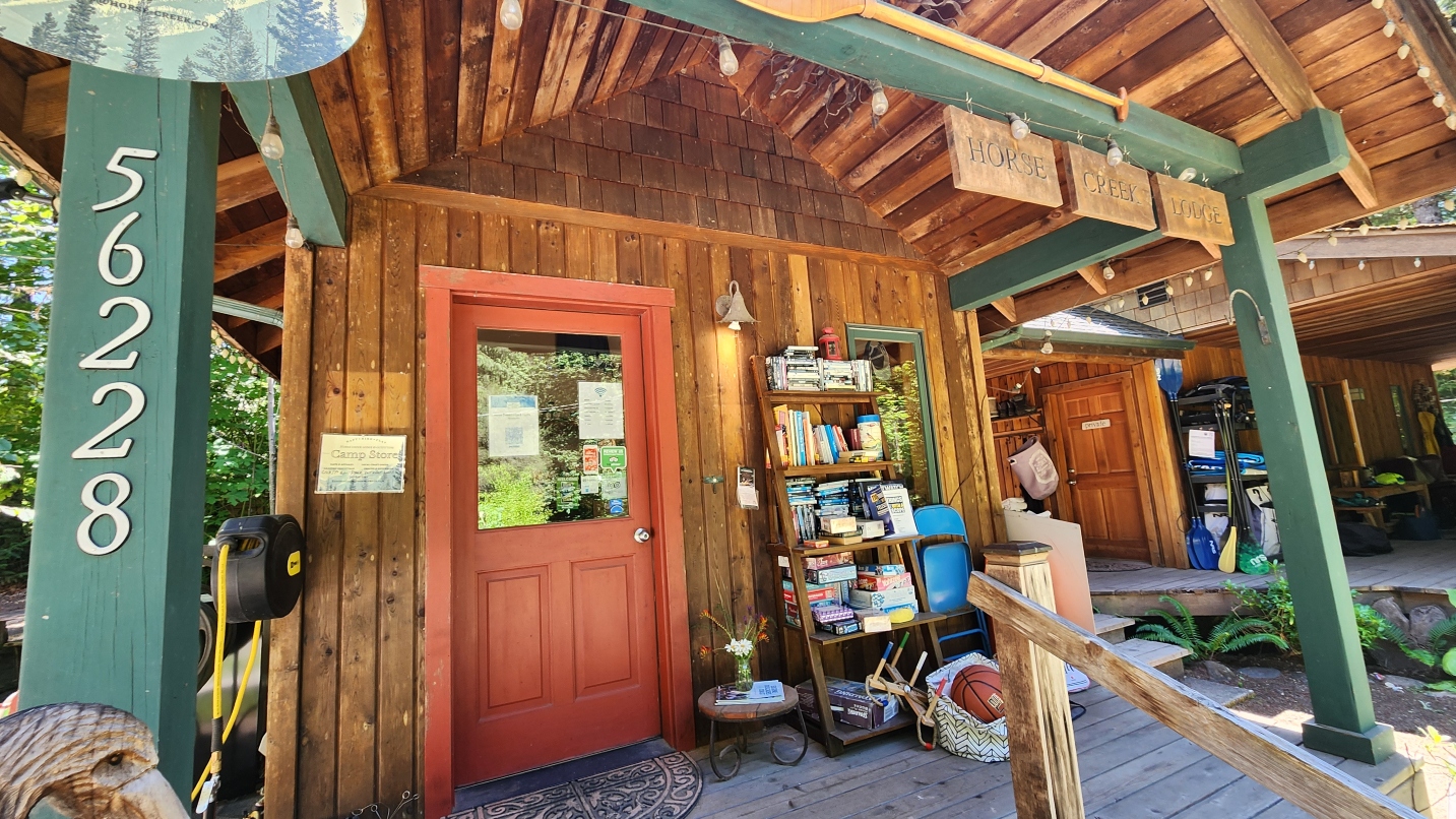 Rustic lodge with green pillars and red door, bookshelf and lights strung across a wooden sign that says Horse Creek Lodge