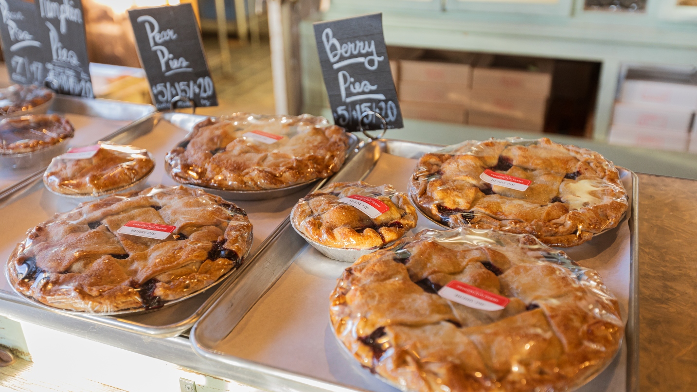 A selection of fresh pies in a bakery case with labels, wrapped in plastic